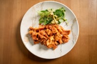 A plate of crispy “oreja brava” served with a fresh watercress salad, presented on a white plate on a wooden table. The