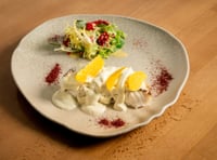 Plato de merluza en salsa cremosa con pilpil de cítricos, acompañado de finas láminas de limón amarillo y una fresca