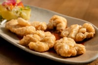 Plato de kokotxas de bacalao crujientes servidas en una tabla de madera, con una textura dorada y apetecible. Acompañadas en