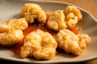 Des kokotxas de morue croustillantes, présentées sur un plateau en papier, dorées et à la texture moelleuse. Ce plat se