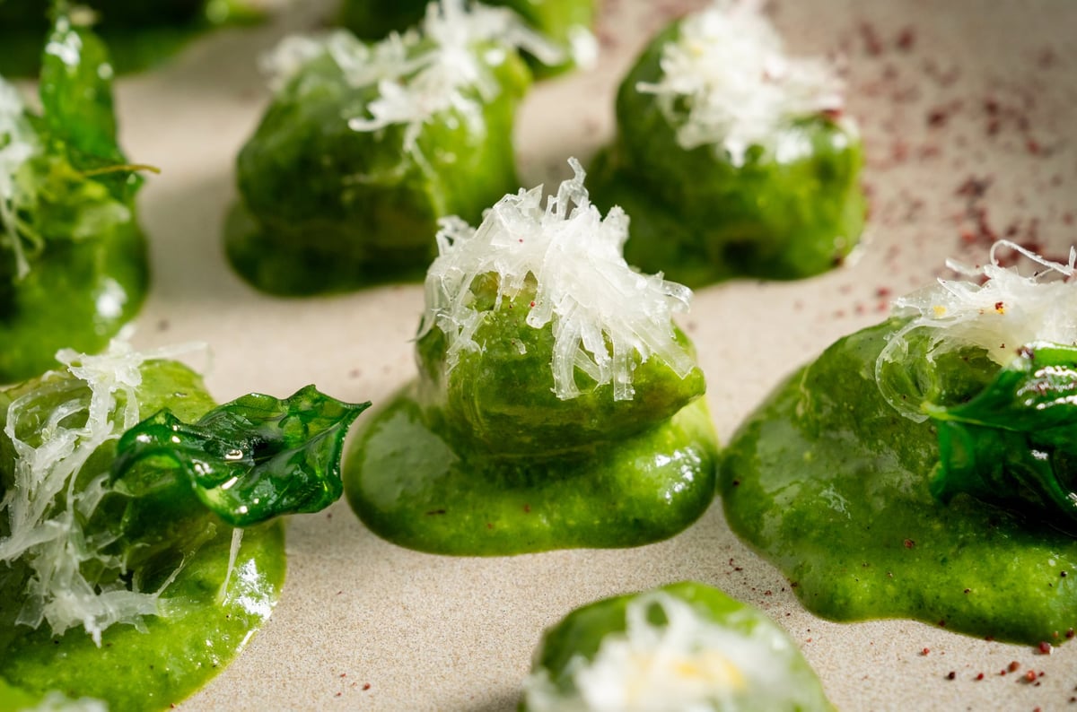 Chestnut gnocchi topped with a crispy layer of grated cheese, arranged on a rustic platter. The vibrant green texture of the