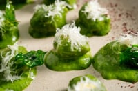 Chestnut gnocchi topped with a crispy layer of grated cheese, arranged on a rustic platter. The vibrant green texture of the