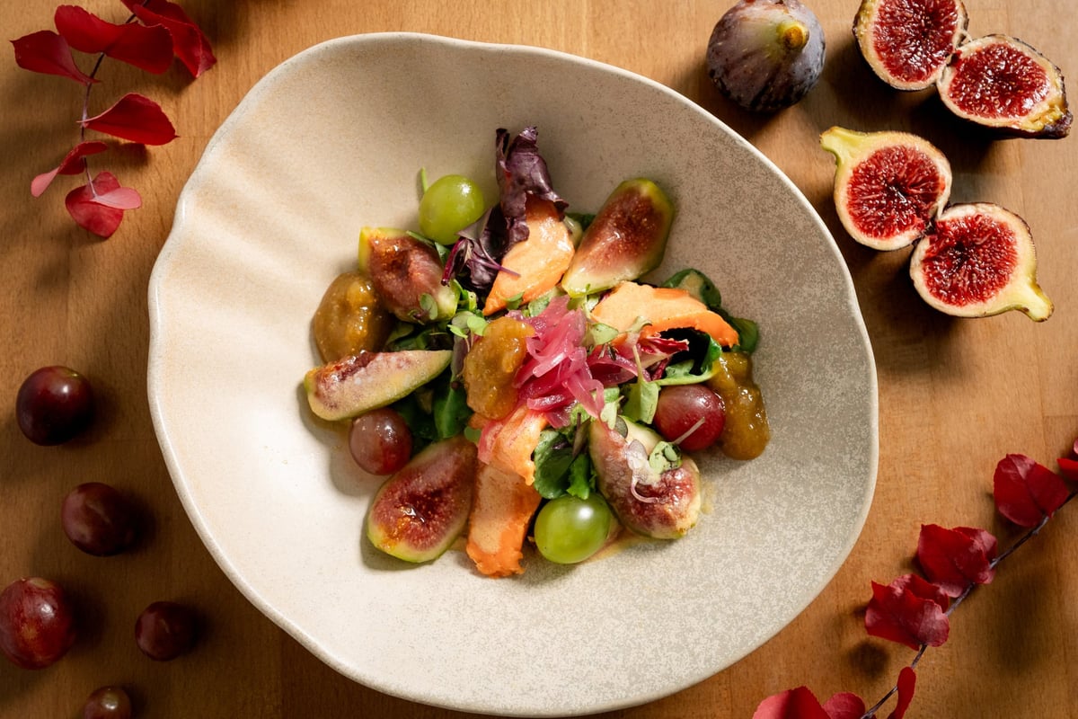 Salade fraîche servie dans un bol, composée de figues caramélisées, de morceaux de poire, de grenade, de roquette et de