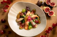 Salade fraîche servie dans un bol, composée de figues caramélisées, de morceaux de poire, de grenade, de roquette et de