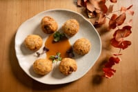 A plate of oxtail croquettes presented on a white tray atop a wooden table, served with sauce and garnished with