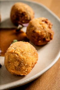 Golden, crispy oxtail croquettes, served on a paper tray on a wooden table. They have a crispy exterior and a creamy