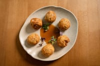 A plate of oxtail croquettes presented on a white ceramic platter on a wooden table. The croquettes have a crispy, golden