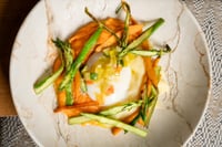 A dish of free-range eggs served in a clay pot, accompanied by strips of roasted bell pepper, green asparagus, and zucchini.