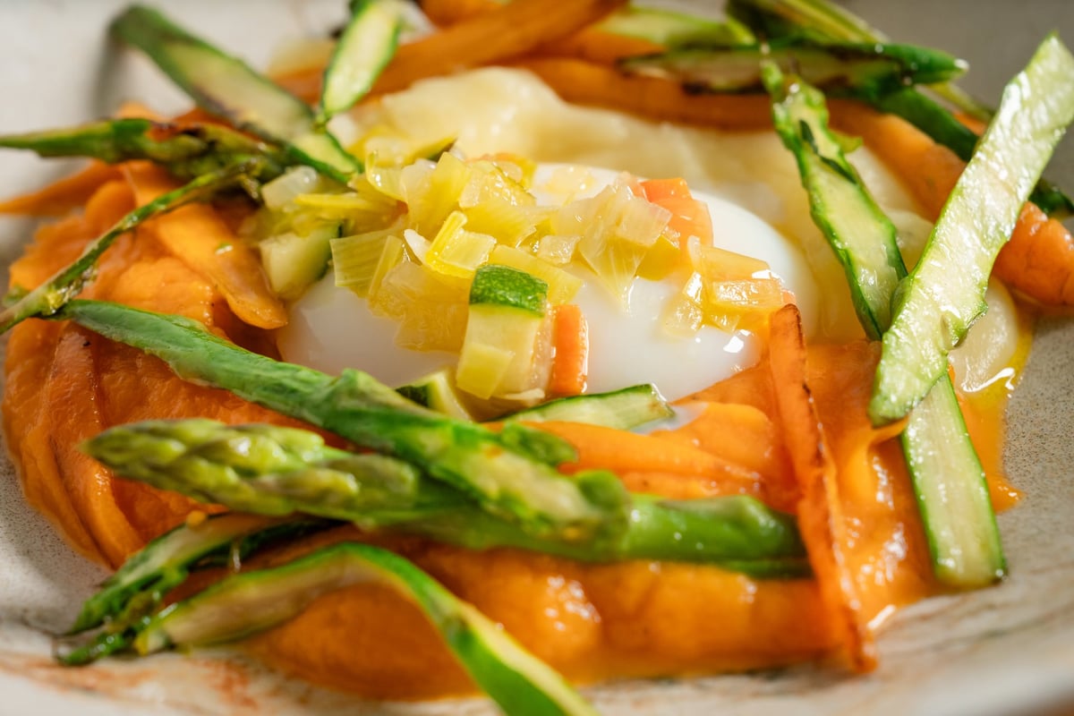A free-range egg served with pieces of caramelized pumpkin and sautéed zucchini sticks, drizzled with a glossy sauce. The