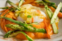 Un œuf fermier servi avec des morceaux de potiron caramélisé et des bâtonnets de courgette sautés, nappés d'une sauce