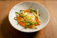Assiette d'œuf fermier servie dans un bol en céramique blanche aux détails rustiques, accompagnée d'asperges vertes et de